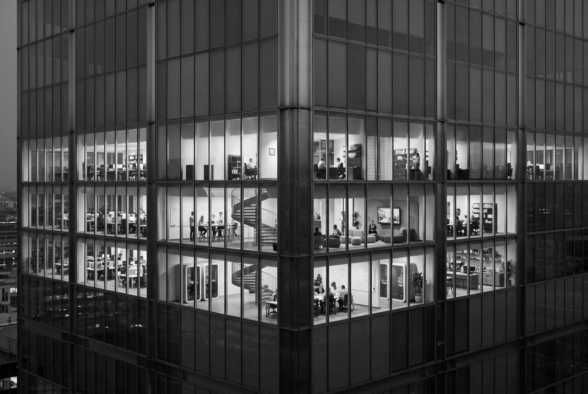 A corner office tower at dusk, its floors lit and at work.